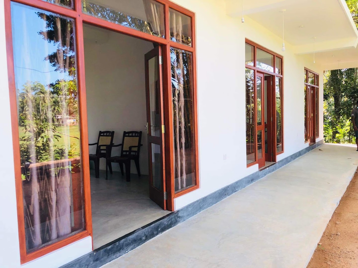 White villa veranda with timber-framed doors opening toward a tropical garden
