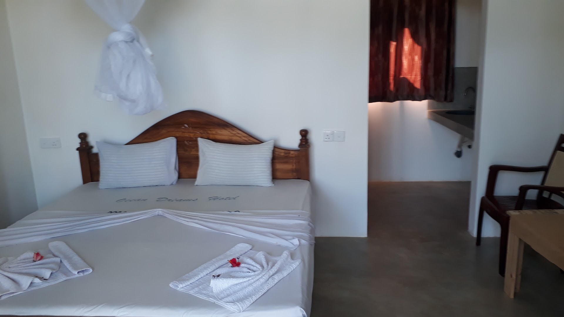 Clean white room with a timber bed, seating, and wash area